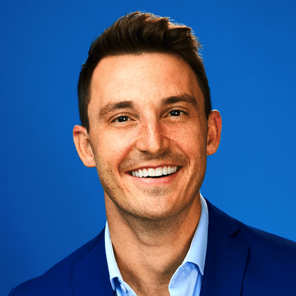 Alex Weber. Headshot of Alex webber wearing a dark blue suit over a light blue shirt. He is posing in front of a blue backdrop.