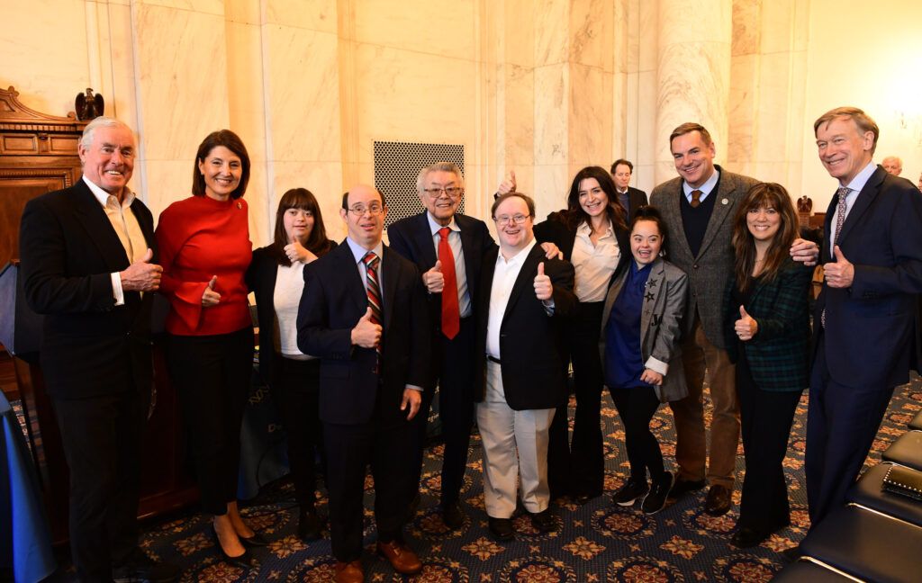 Madison Tevlin posing with a group of people in a large room at the 2024 GLOBAL DC Fly-In with the Global Down Syndrome Foundation.