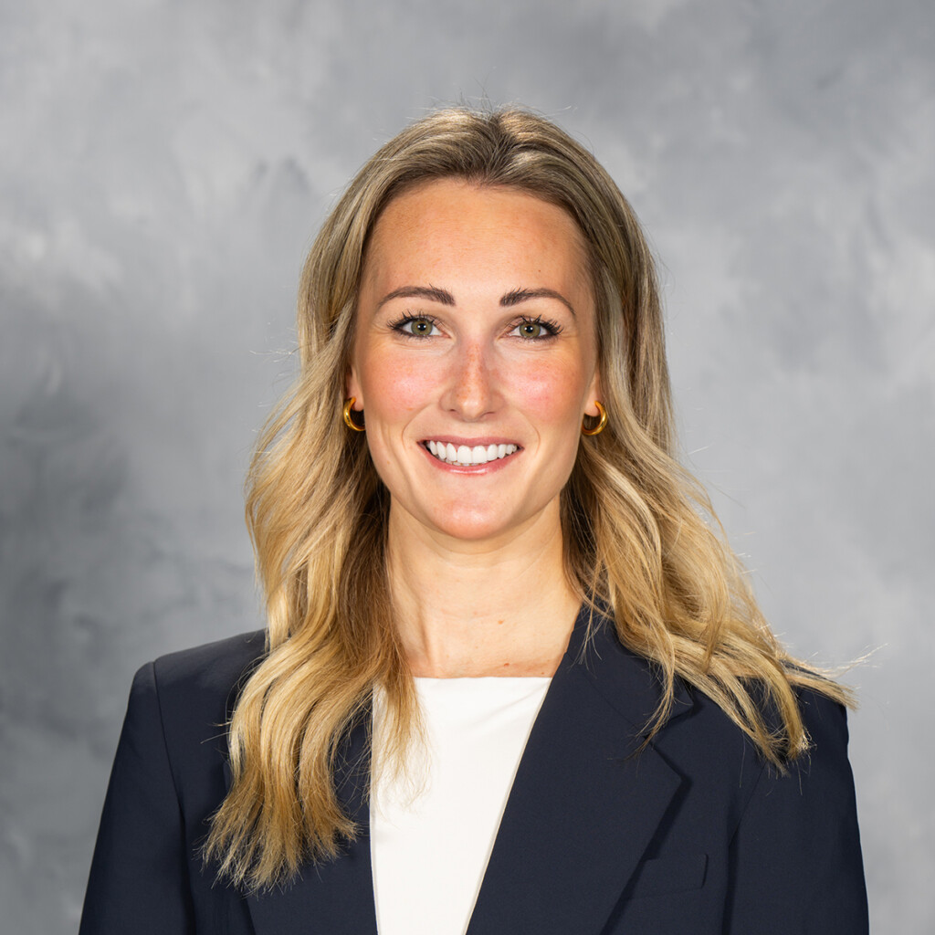 Jessica Campbell. Headshot of Jessica Campbell wearing a black jacket over a white shirt. She is posing in front of a grey studio background.