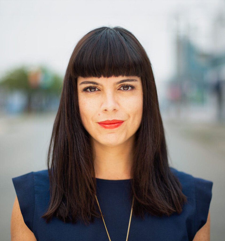 Lital Marom. Headshot of Lital Marom wearing a navy short sleeve top. She is posing outside and the background is blurry.