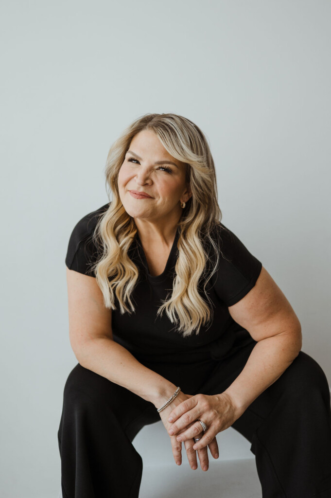 Headshot of Dr. Jody Carrington sitting in front of a solid white background. She is smiling at the camera and is wearing a black t-shirt and black pants.