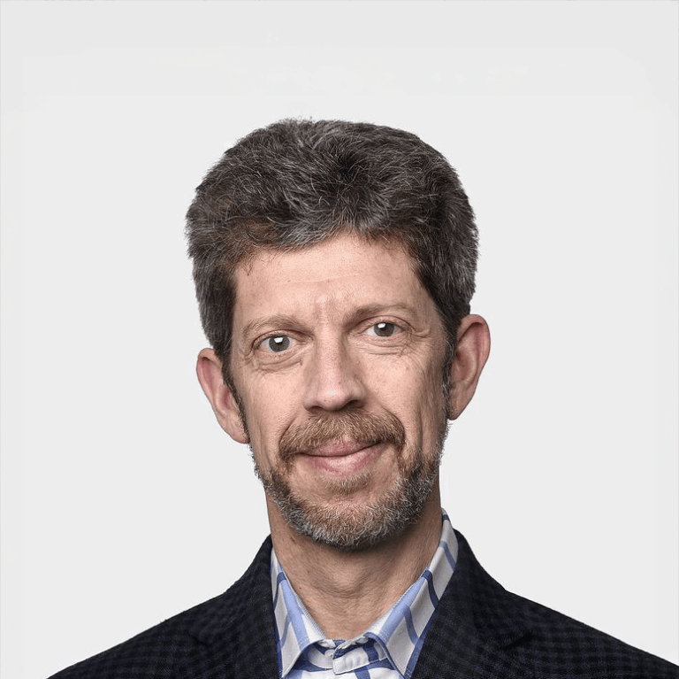 Rob Carrick. Headshot of Rob Carrick wearing a dark suit jacket over a collared shirt. He is posing in front of a bright white backdrop.