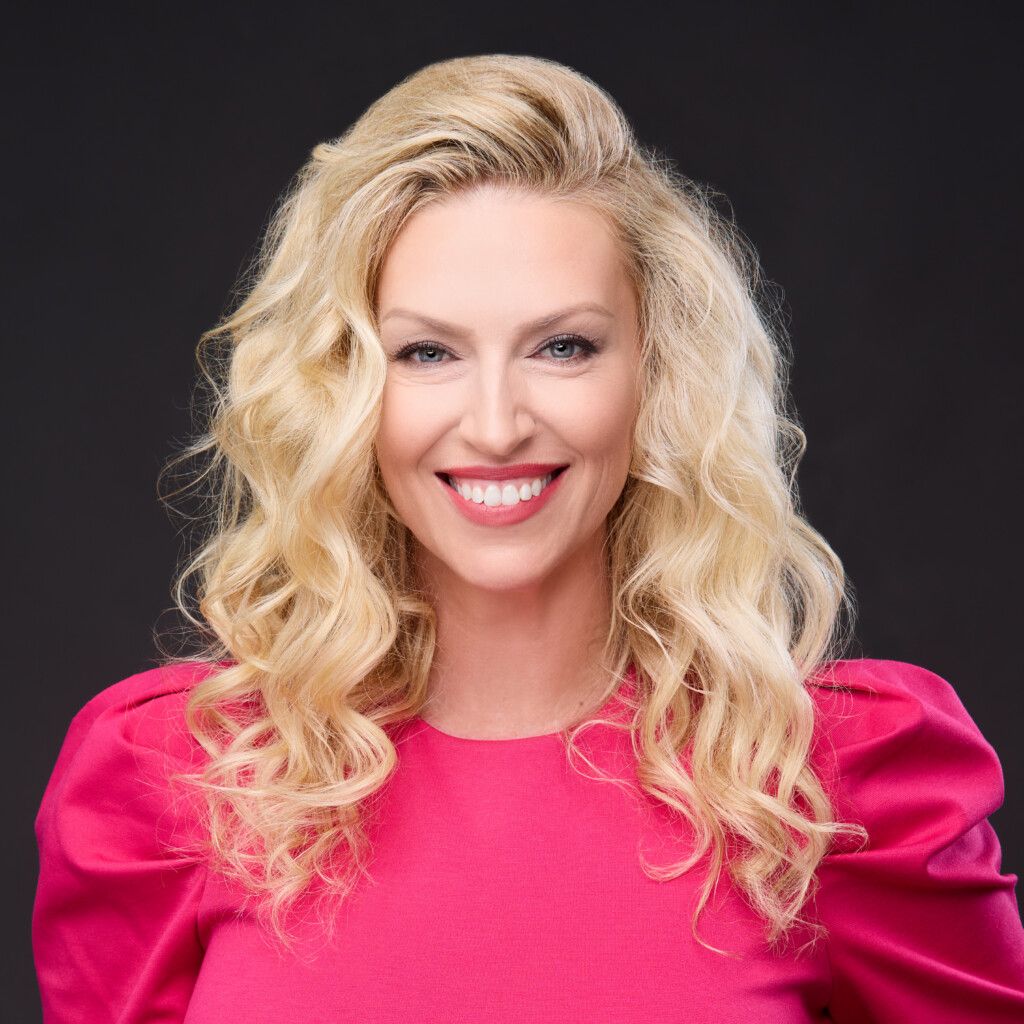 Sara Ross' headshot in front of a solid black background. She is smiling and is wearing a hot pink blouse.