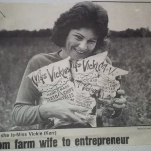 Black and white newspaper clipping of founder and creator of Miss Vickie's, Vickie Kerr. Vickie is holding 4 bags of Miss Vickie's chips in her arms.