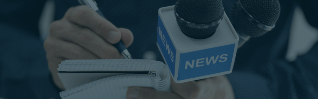 Close up image of a journalist writing on a notepad with a pen. They are holding a microphone, with the word "NEWS" on it, in the other hand.