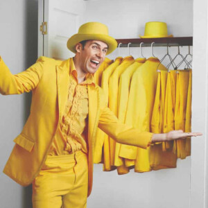 Image of Jesse Cole wearing a full yellow suit and standing in front of a closet full of yellow suits.