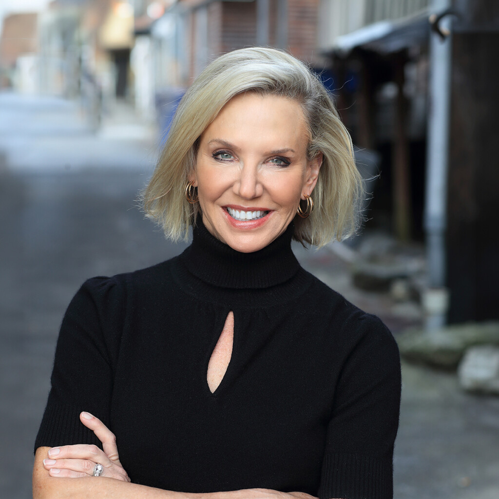 Meridith Elliott Powell Headshot. She is posing outside with her arms crossed, wearing a black turtleneck top.