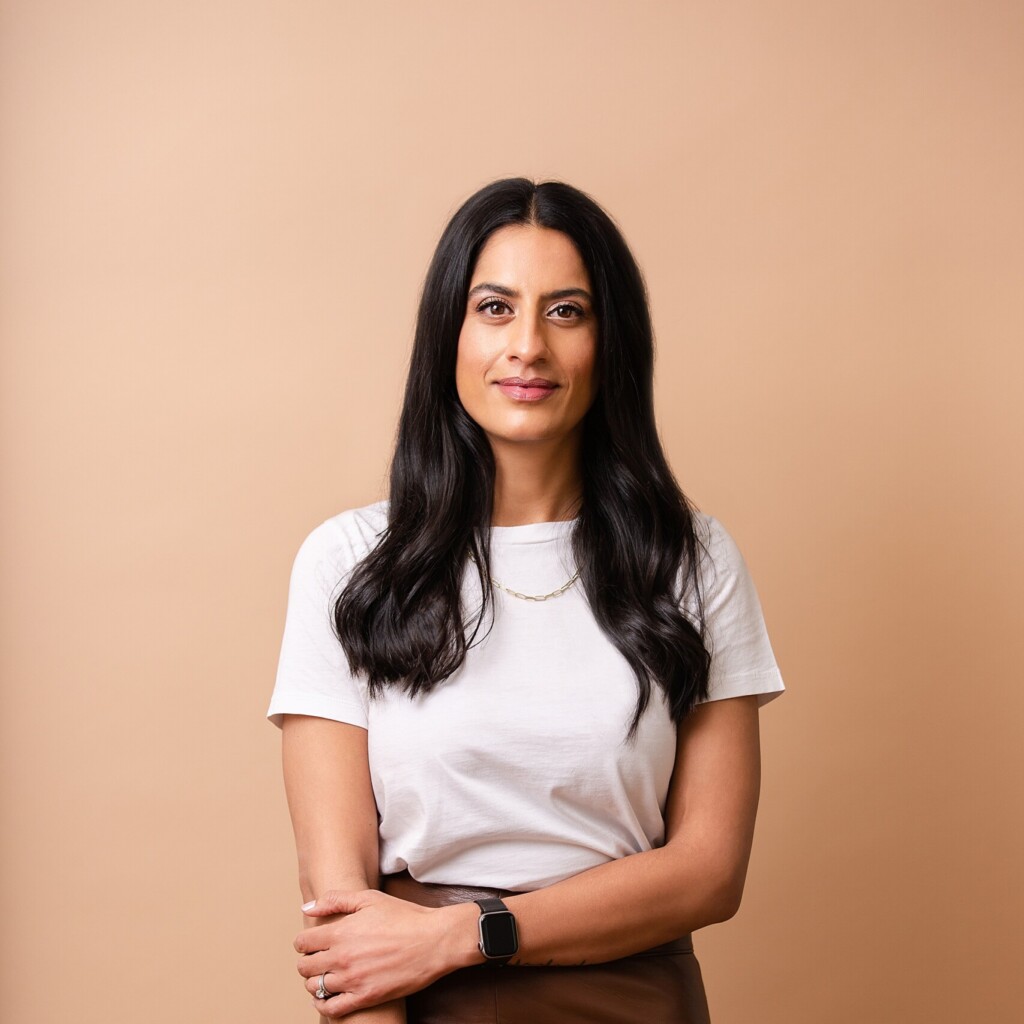 Headshot of Dr. Shazma Mithani standing in front of an light orange-coloured backdrop. She is wearing a white t-shirt and long brown leather skirt.